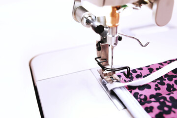 close up on individual pink protective cotton face mask with screen print that is produced with an industrial high-speed sewing machine in bright working light - sustainable pandemic fashion concept