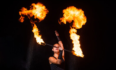 Sexy girl artist twirl burning batons during sparkling fire performance in darkness, lighting