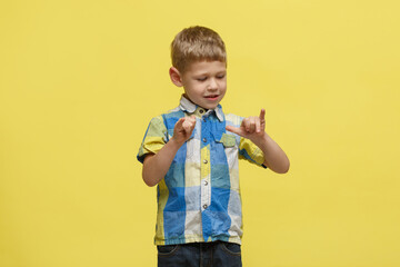 Little cute boy in a bright shirt considers fingers on his hand isolated on a yellow background.