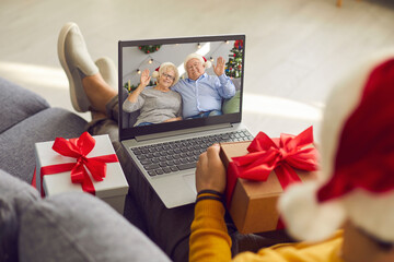 Grown-up son holding present and video calling his senior parents on Christmas Day