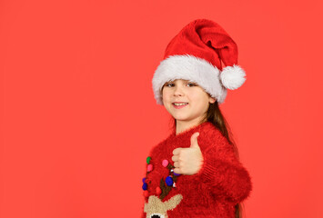 little santa helper show thumb up. small girl santa claus hat red background. copy space. ready for new year party. christmas my favorite holiday. love winter holidays. in xmas mood