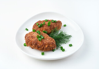 White plate with fried cutlets and herbs on a white background. Side view. The concept of cooking.