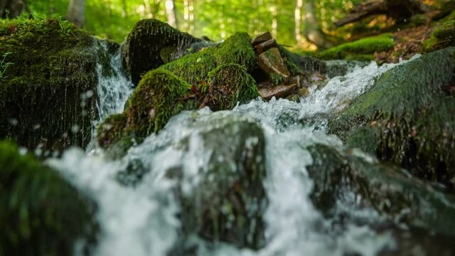 Purest mountain river in the forest. Stream of water moves between the stones covered with moss. HDR slow motion gimbal shot. Nature background series