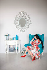 A beautiful brunette woman in  dress sits in blue chair. image with selective focus