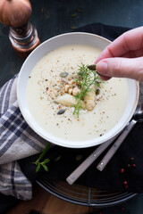 Closeup view of a bowl of asparagus cream soup with a pipe being held by a woman hand at the front.