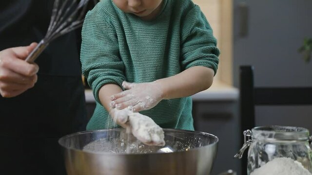 A boy child and mother preparing dough in a warm cozy kitchen on a wooden table. Family life and hobbies concept.