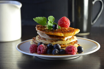 Pancakes with berries and maple syrup with raspberries and blueberries on a black background