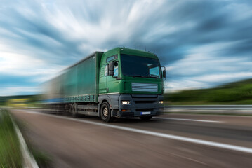 Green Lorry truck speeding on freeway at sunset, motion blurred.