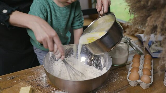 A boy child and mother preparing dough in a warm cozy kitchen on a wooden table. Family life and hobbies concept.