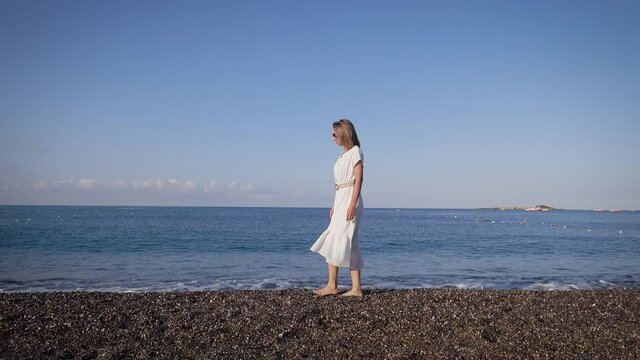 Slender young woman against the background of the Mediterranean Sea. Walk on a summer day along the coastline.