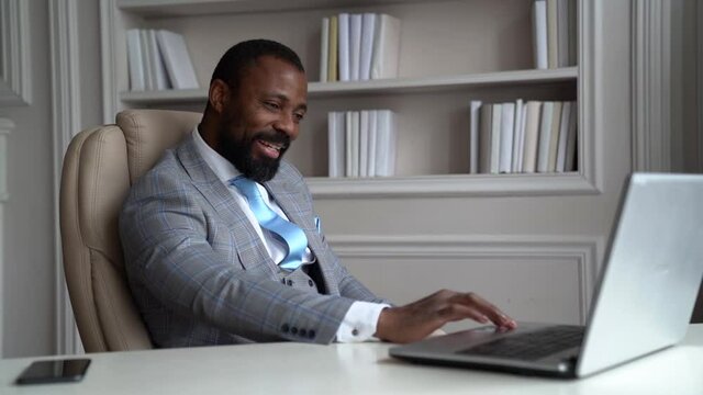 male boss is communicating with team by online chat at screen of notebook, sitting in his luxury office