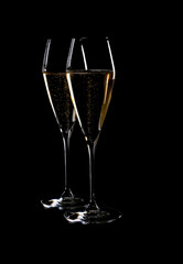Two Elegant Crystal Champagne Flutes Filled with Sparkling White Wine Isolated on Black Background