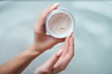 Top view of a pink cream or face mask in the hands of a girl. A woman holds a jar of cream on the background of foam in the bath. Spa procedure, body care, skin health product