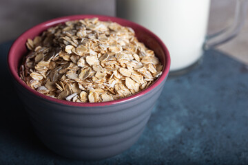 Dry rolled oatmeal in a bowl with milk on dark blue background. Healthy cereal flakes in a ceramic bowl and glass of milk close-up.