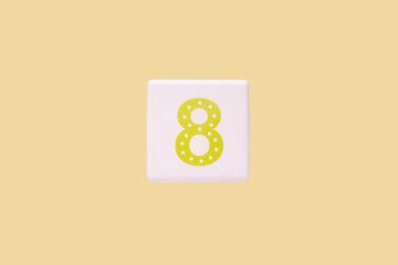 Fototapeta na wymiar Close-up photo of a white plastic cube with a yellow number 8 on a yellow background. Object in the center of the photo