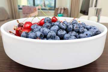 Raw juicy berries of sweet cherry and blueberry in a white ceramic dish