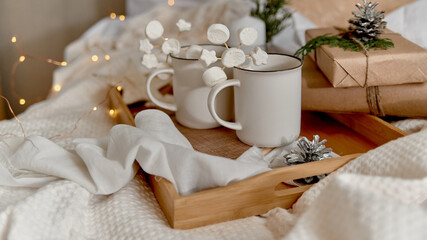 Obraz na płótnie Canvas Hot cocoa with marshmallow in a white ceramic mug, on a wooden tray and wrapped boxes. The concept of cosy holidays and New Year. Selective focus