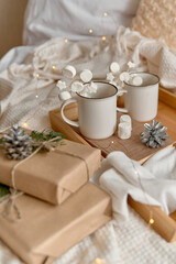 Hot cocoa with marshmallow in a white ceramic mug,  on a wooden tray and wrapped boxes. The concept of cosy holidays and New Year. Selective focus