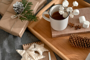 Christmas background with mug of hot  cocoa with marshmallow on wooden tray, Notepad with pencil, wrapped boxes and decoration. Cozy mood holiday. Hygge. Letter To Santa Claus concept. Selective focus