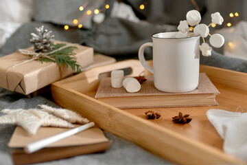 Fototapeta na wymiar Christmas background with mug of hot cocoa with marshmallow on wooden tray, Notepad with pencil, wrapped boxes and decoration. Cozy mood holiday. Hygge. Letter To Santa Claus concept. Selective focus