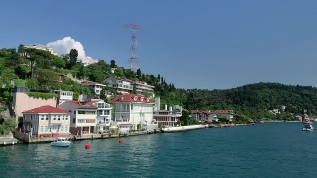 Footage of a yacht passing on Bosphorus, mansions at upscale neighborhood called "Kandilli" in Istanbul. It is a beautiful scene in a sunny summer day. Camera moves forward.