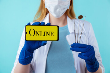 Young female dentist in mask and medical coat holding instruments and phone. Appointment online cocnept