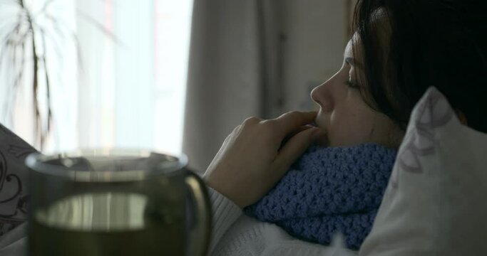 Sick Woman Measures Temperature with Thermometer while Lying in Bed in front of Window in Bedroom 4K