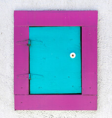 Wooden turquoise door with magenta frame mounted on outdoor wall.