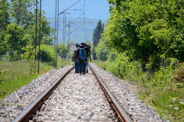 Group of migrants walking on train tracks in countryside. Refugees on their  way to EU.  Rear view...