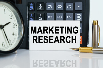 On the table there is a clock, a pen, a calculator and a business card on which the text is written - MARKETING RESEARCH