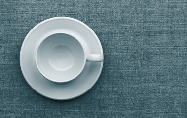 White cup and saucer on natural linen fabric. toned in blue-green, tidewater green. flat lay. space