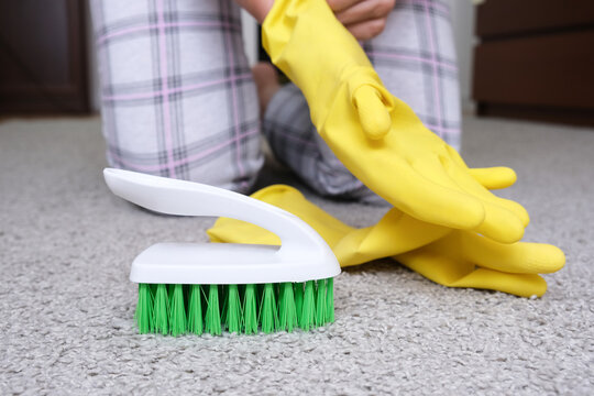 Woman in yellow gloves with a green brush cleaning and brushing carpet, removing stains and wool from it and doing routine homework