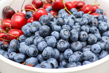 Raw juicy berries of sweet cherry and blueberry in a white ceramic dish, close up
