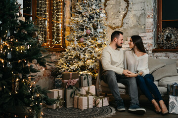 Portrait of a happy young family near a festive Christmas tree. The couple hugs each other tenderly. Good New Year spirit