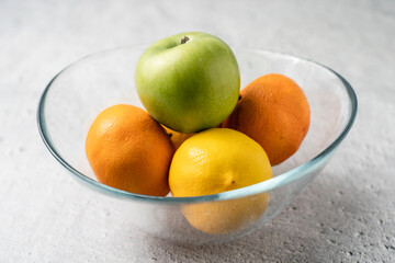 Close up on green apple granny smith with oranges and lemon on marble table in glass bowl - healthy organic eating fresh food rich in vitamins copy space