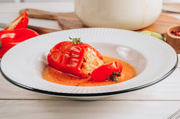Pepper stuffed with minced chicken meat and rice in a white plate on a white wooden table.