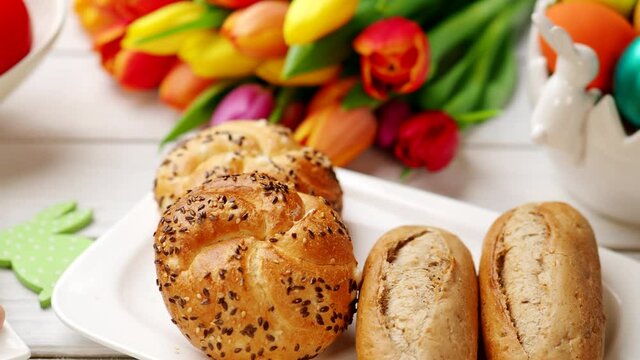 Fresh crusty loaves of bread and bun with ham, eggs, tomatoes, radish on white table in 4K VIDEO. Easter romantic breakfast served with love and tulip bouquet.