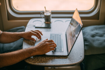 Male hands with a laptop on the table in the train. Close-up.