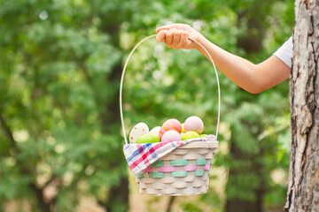 Child hand holding basket full of colorful easter eggs after egg hunt at spring time. Happy Easter...