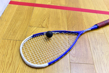 Squash racket and ball on court floor in training club. Sports equipment and sportswear for playing squash. Racquetball on wooden background.