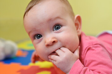 A seven month old baby girl lying on her tummy and sucking her fingers.