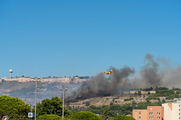 Fototapeta premium fire starts on the hills of Marseille, near Marignane airport. yellow fire-fighting plane is going to throwing water on it. 