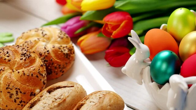 Fresh crusty loaves of bread and bun with ham, eggs, tomatoes, radish on white table in 4K VIDEO. Easter romantic breakfast served with love and tulip bouquet.