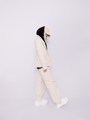 Blonde Girl in white studio. Trendy beige casual outfit with black hoodie details.  Cap, Denim Suit...