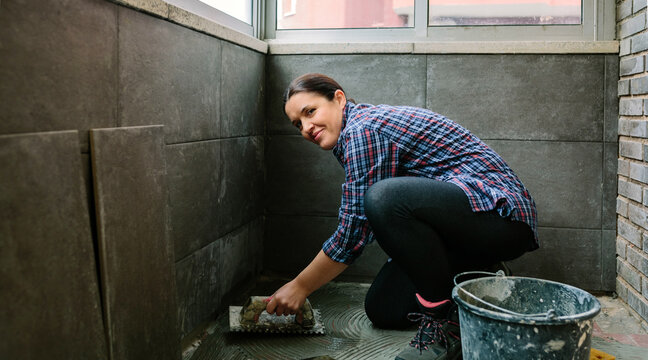 Smiling female mason laying a new tile floor on a terrace