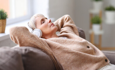 Senior woman listening to music lying on sofa.