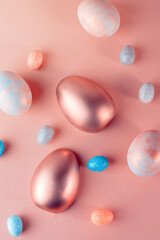 Trendy Easter background with Gold and colored Easter eggs on a light coral color background with copy space. Top view still life. Easter concept.