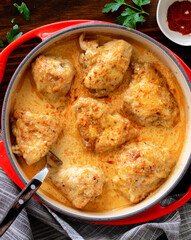 Poulet Gaston Gerard  served in a red cast iron dish sitting on dark wooden background- It is a traditional dish from the French city of Dijon.