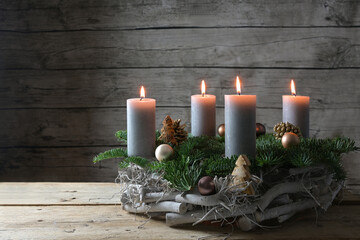 Rustic advent wreath of wood, fir branches and Christmas decoration with four burning candles...