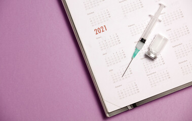 syringe and vaccine with calendar 2021, lilac background